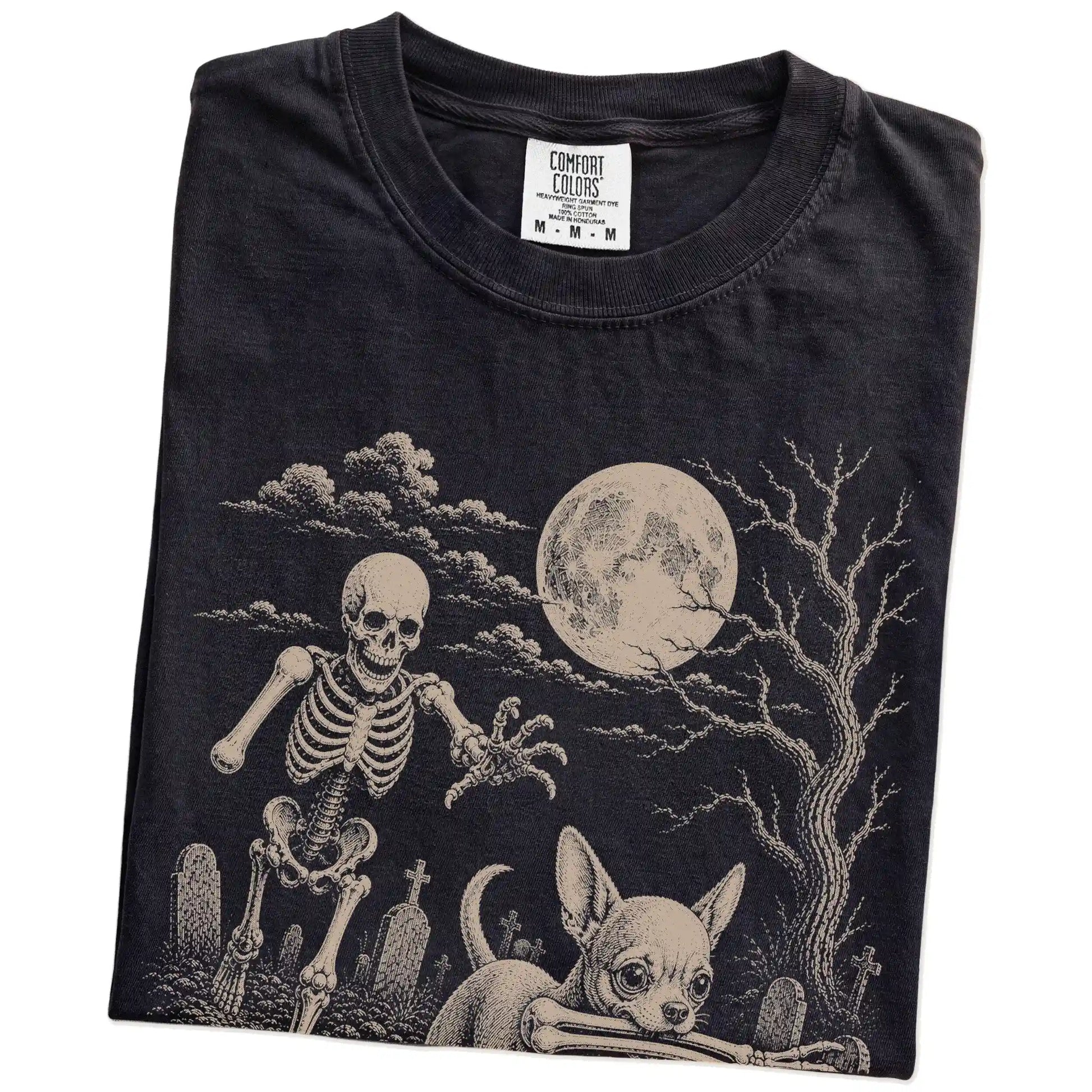 Folded Black Comfort Colors® T-shirt showing Chihuahua running through a moonlit graveyard with a chasing skeleton