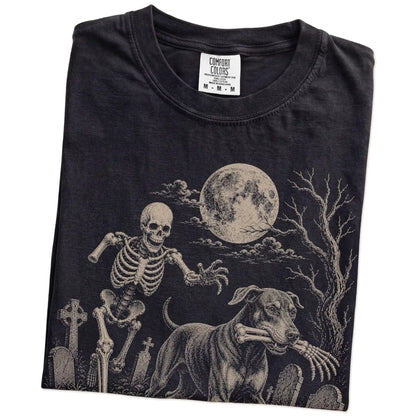 Folded Black Comfort Colors® T-shirt showing Doberman running through a moonlit graveyard with a chasing skeleton