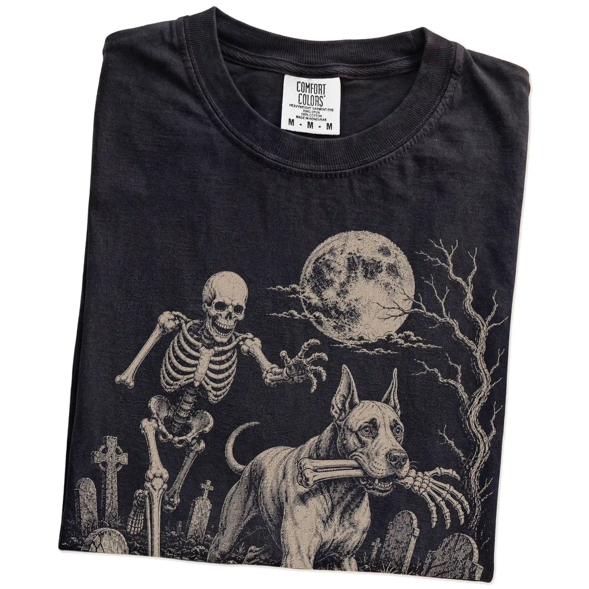 Folded Black Comfort Colors® T-shirt showing Great Dane running through a moonlit graveyard with a chasing skeleton