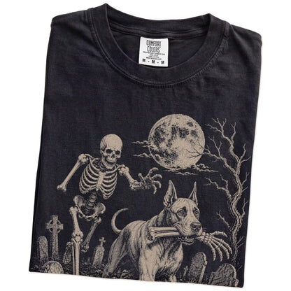 Folded Black Comfort Colors® T-shirt showing Great Dane running through a moonlit graveyard with a chasing skeleton