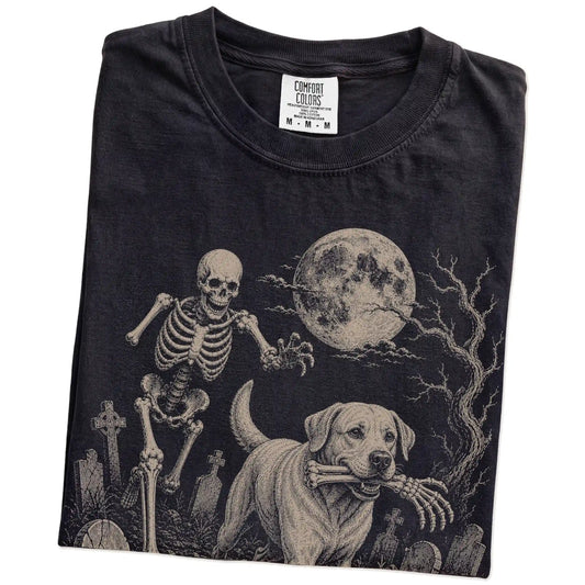Folded Black Comfort Colors® T-shirt showing Labrador Retriever running through a moonlit graveyard with a chasing skeleton