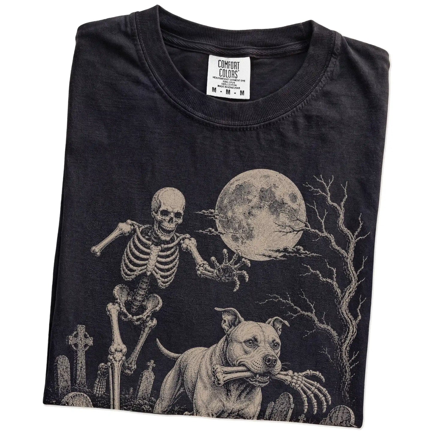 Folded Black Comfort Colors® T-shirt showing Pitbull running through a moonlit graveyard with a chasing skeleton