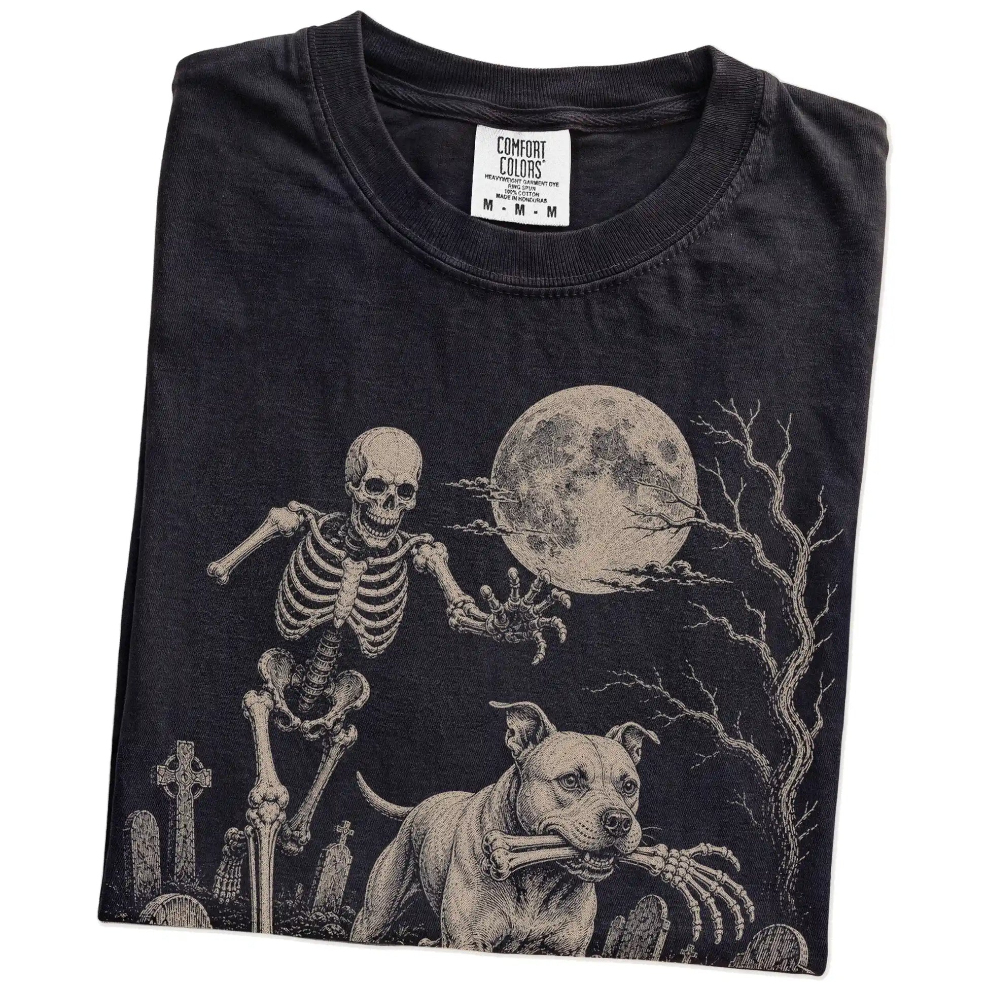 Folded Black Comfort Colors® T-shirt showing Pitbull running through a moonlit graveyard with a chasing skeleton