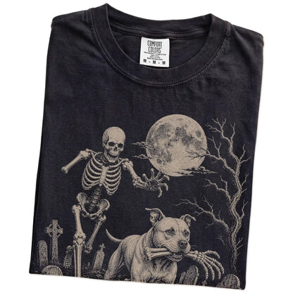 Folded Black Comfort Colors® T-shirt showing Pitbull running through a moonlit graveyard with a chasing skeleton