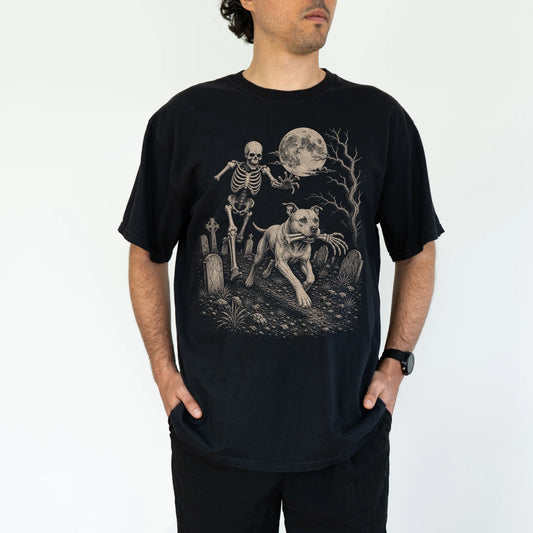 Model wearing a Black Comfort Colors® T-shirt showing Pitbull running through a moonlit graveyard with a chasing skeleton