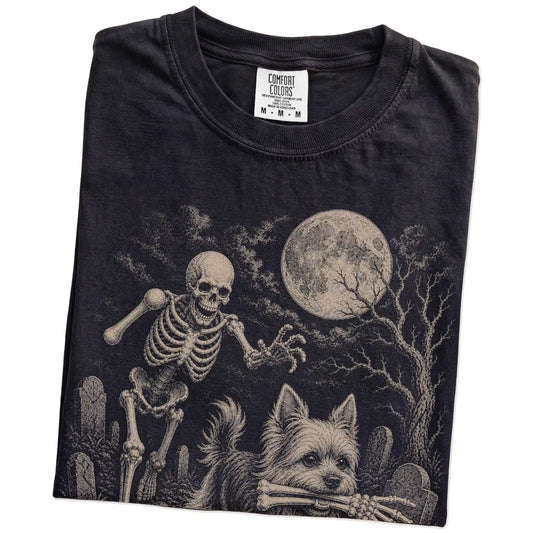Folded Black Comfort Colors® T-shirt showing Yorkie running through a moonlit graveyard with a chasing skeleton