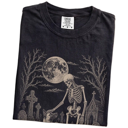 Folded Black Comfort Colors® T-shirt showing Belgian Malinois sharing a quiet cemetery moment with a friendly skeleton