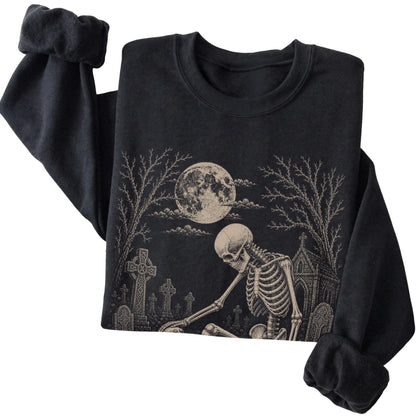 Folded Black sweatshirt with a skeleton petting a Cavalier in a graveyard
