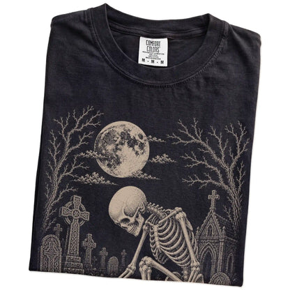 Folded Black Comfort Colors® T-shirt showing Chihuahua sharing a quiet cemetery moment with a friendly skeleton