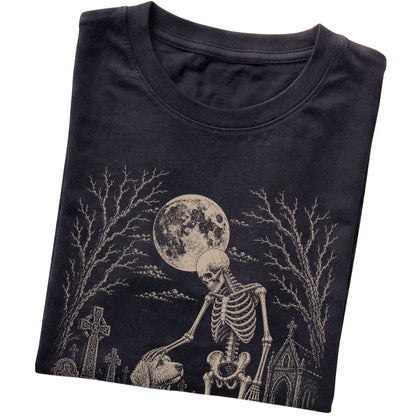 Folded Black T-shirt with a skeleton petting a Goldendoodle in a graveyard