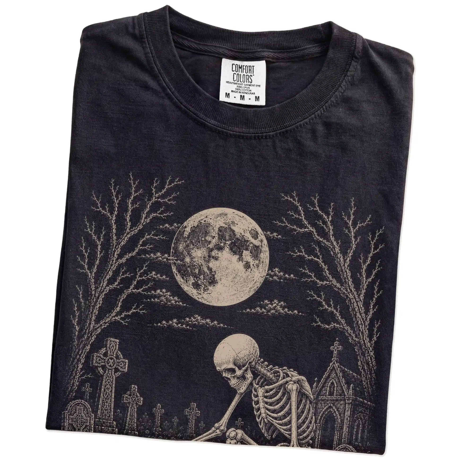 Folded Black Comfort Colors® T-shirt showing Pomeranian sharing a quiet cemetery moment with a friendly skeleton
