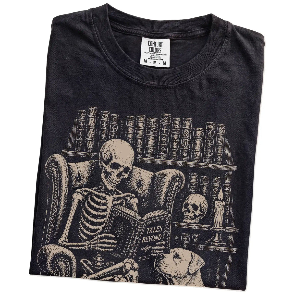 Folded Black Comfort Colors® T-shirt showing skeleton reading in a library beside a American Bulldog