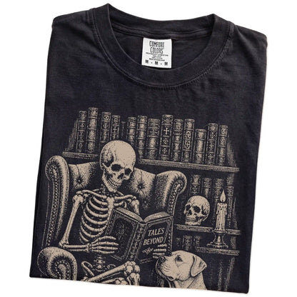 Folded Black Comfort Colors® T-shirt showing skeleton reading in a library beside a American Bulldog