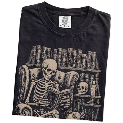 Folded Black Comfort Colors® T-shirt showing skeleton reading in a library beside a Blue Heeler