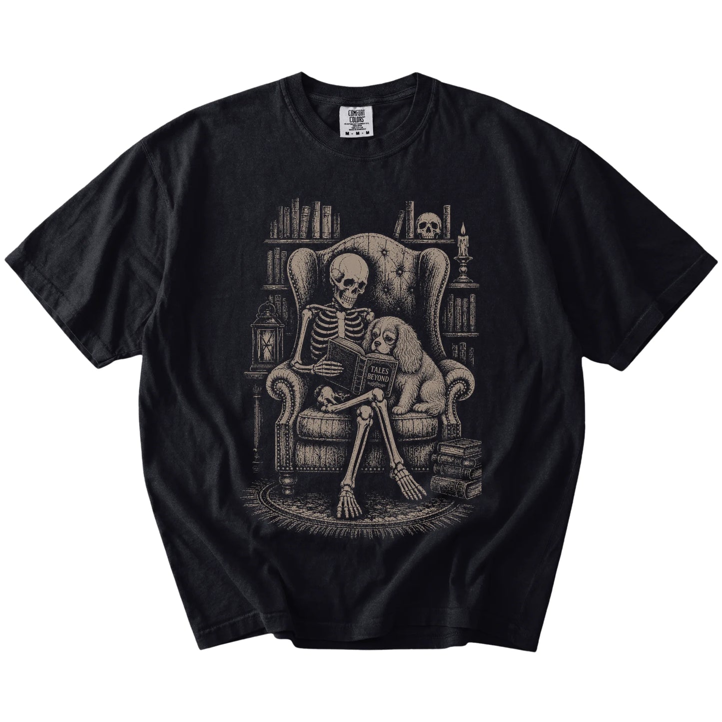 Skeleton reading in a library beside a Cavalier King Charles Spaniel on a Black Comfort Colors® T-shirt