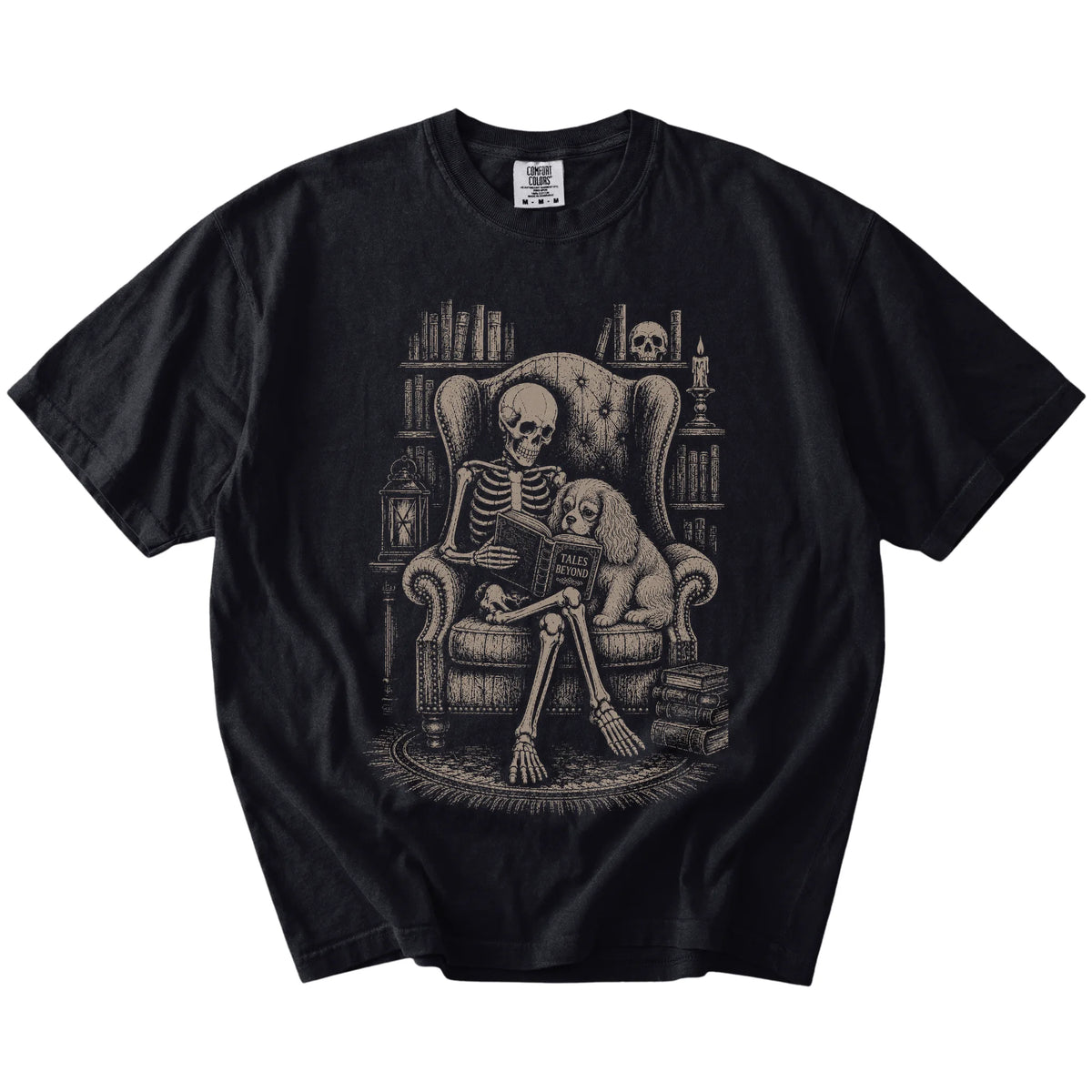 Skeleton reading in a library beside a Cavalier King Charles Spaniel on a Black Comfort Colors® T-shirt