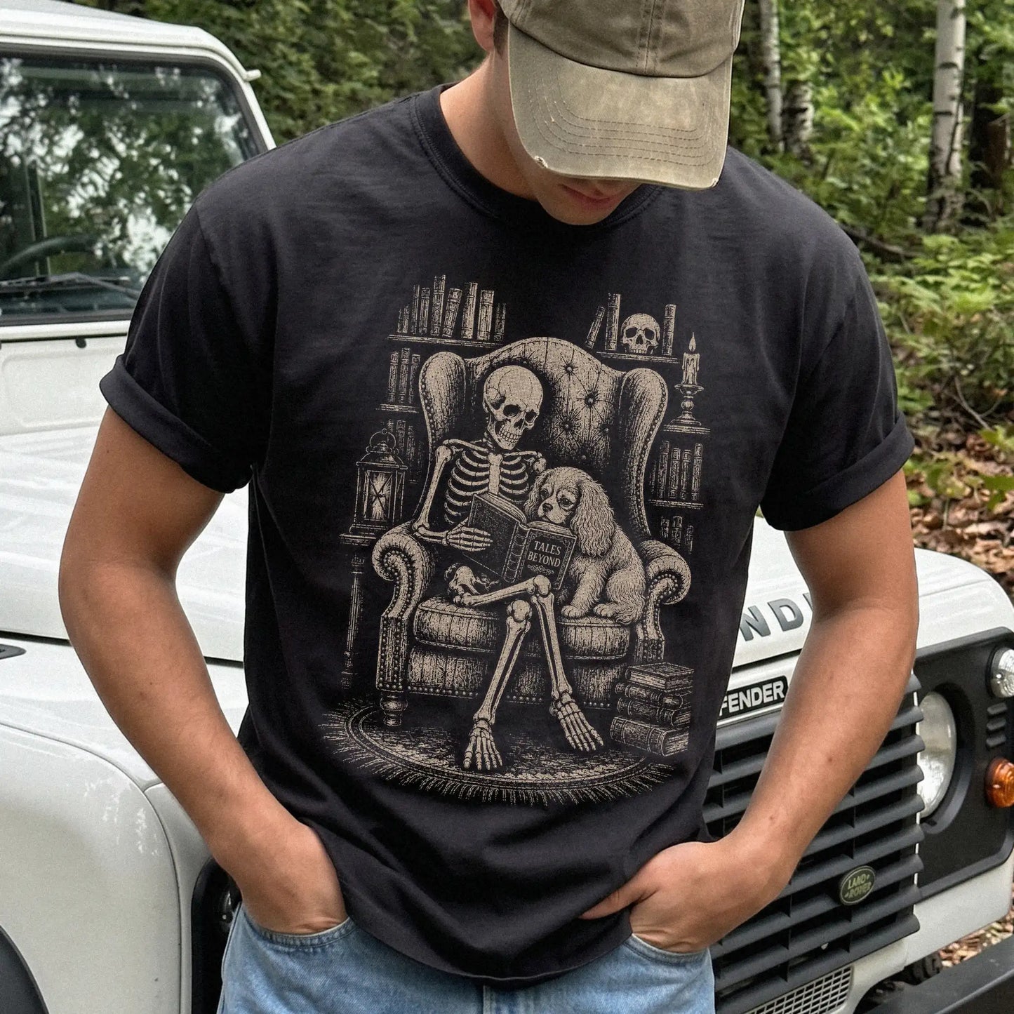 Model wearing a Black Comfort Colors® T-shirt showing skeleton reading in a library beside a Cavalier King Charles Spaniel