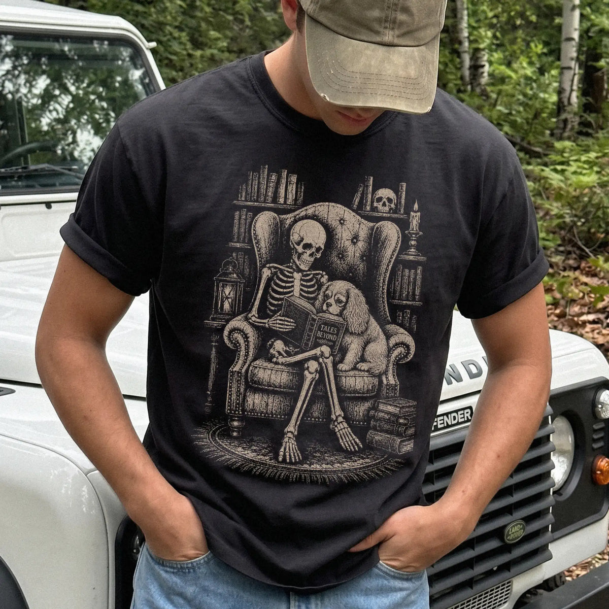 Model wearing a Black Comfort Colors® T-shirt showing skeleton reading in a library beside a Cavalier King Charles Spaniel