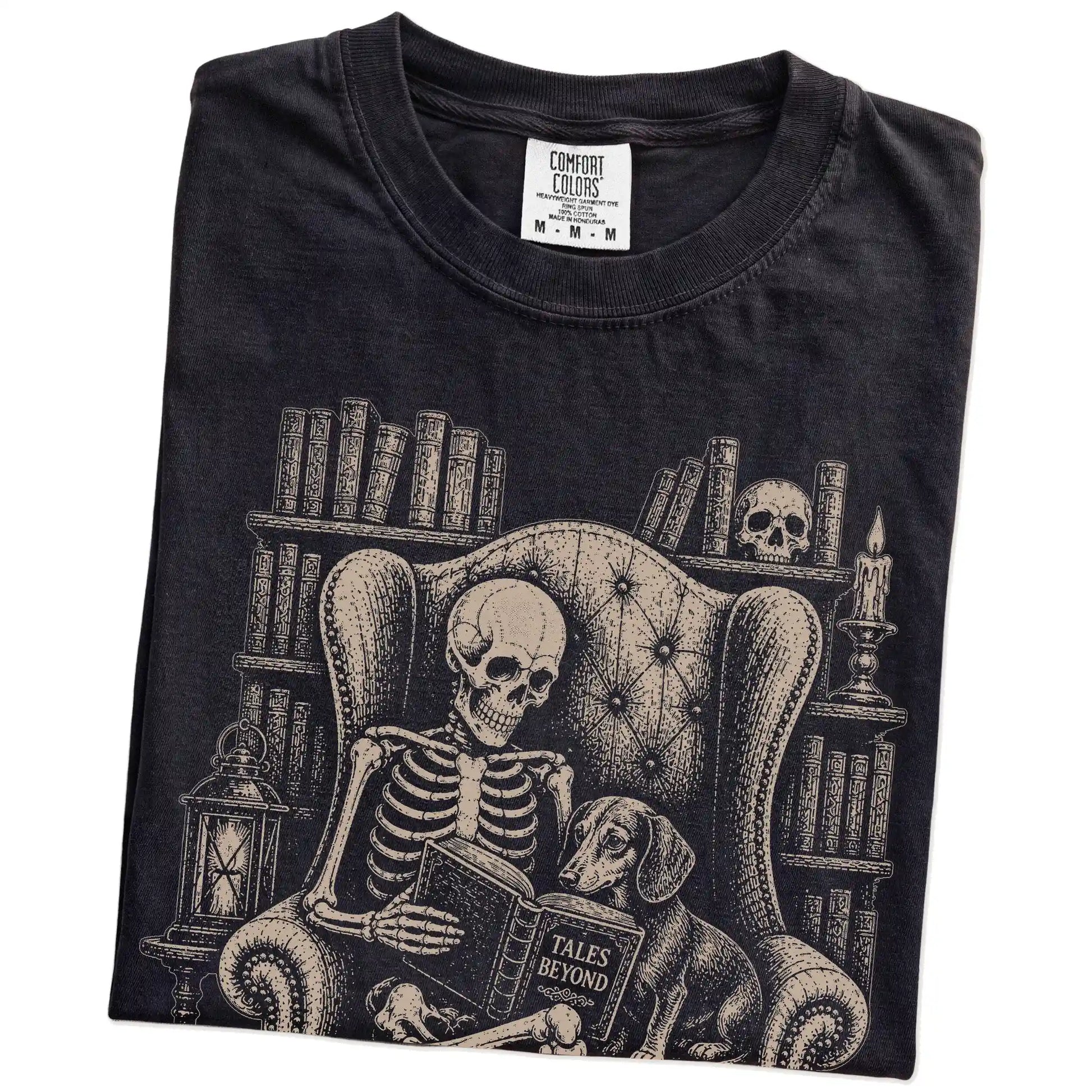 Folded Black Comfort Colors® T-shirt showing skeleton reading in a library beside a Dachshund