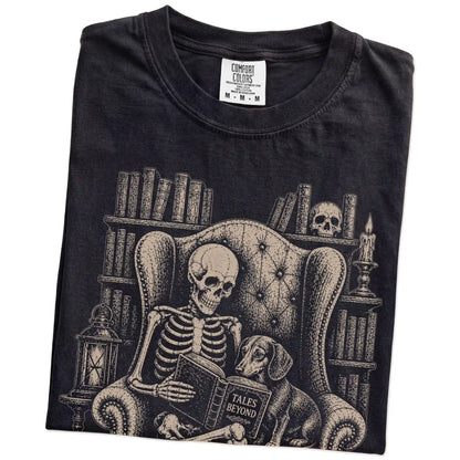 Folded Black Comfort Colors® T-shirt showing skeleton reading in a library beside a Dachshund