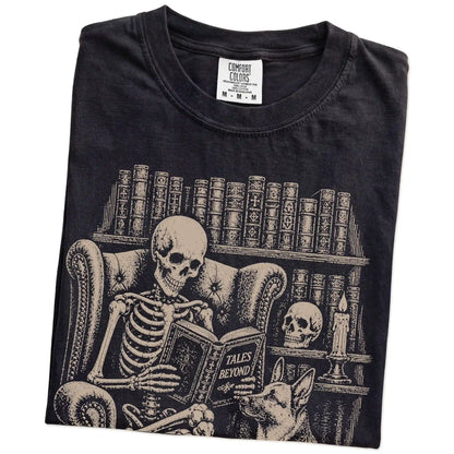 Folded Black Comfort Colors® T-shirt showing skeleton reading in a library beside a German Shepherd