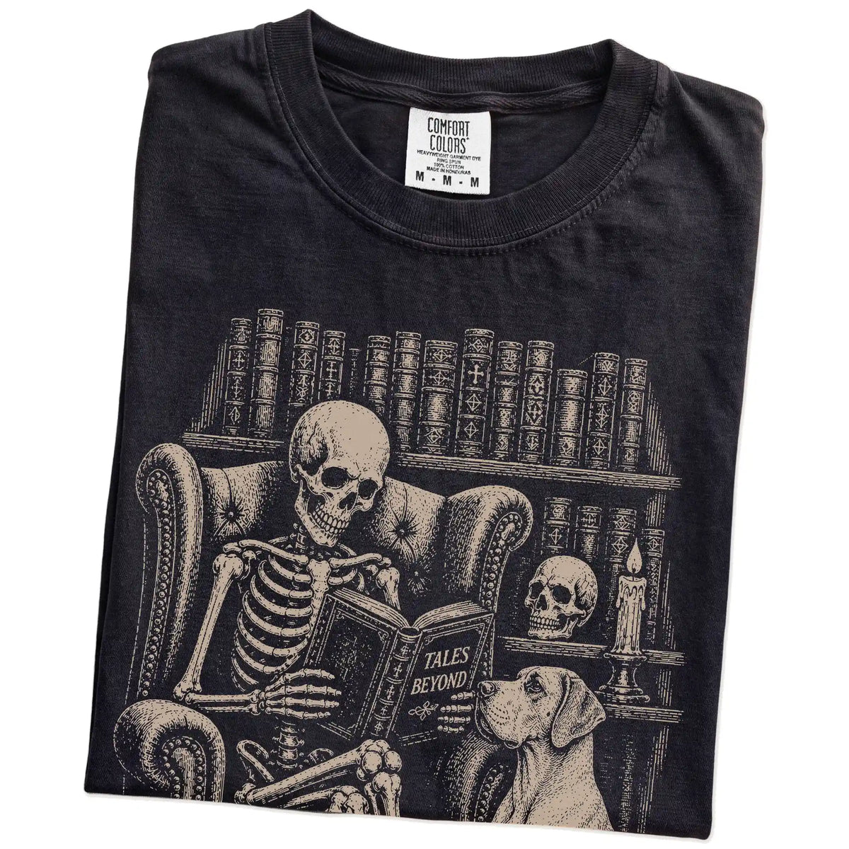 Folded Black Comfort Colors® T-shirt showing skeleton reading in a library beside a Great Dane