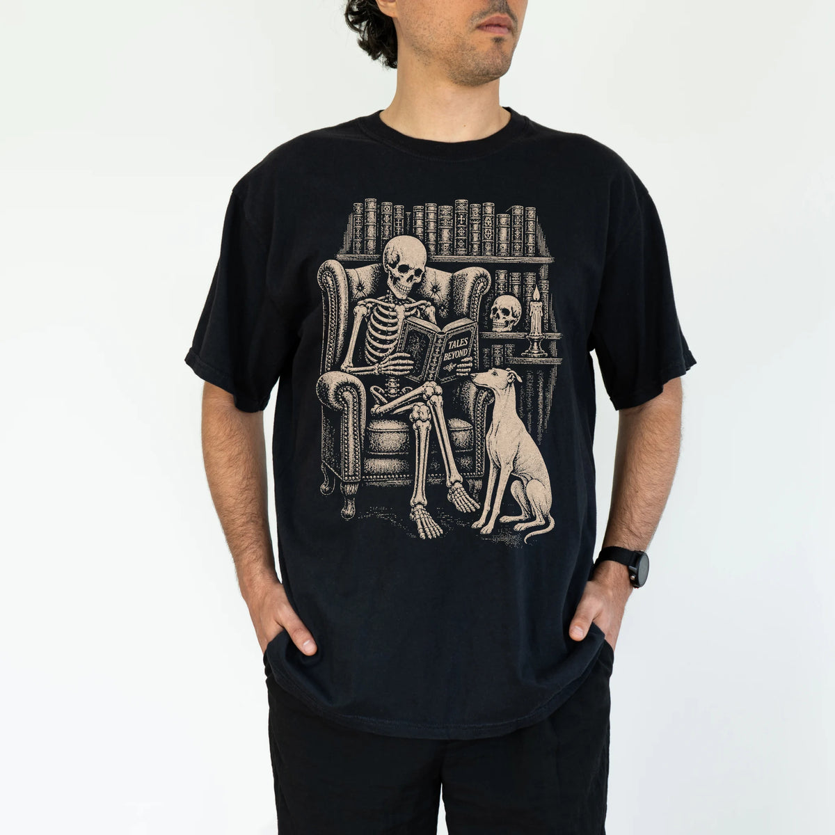 Model wearing a Black Comfort Colors® T-shirt showing skeleton reading in a library beside a Greyhound