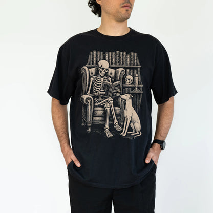 Model wearing a Black Comfort Colors® T-shirt showing skeleton reading in a library beside a Greyhound