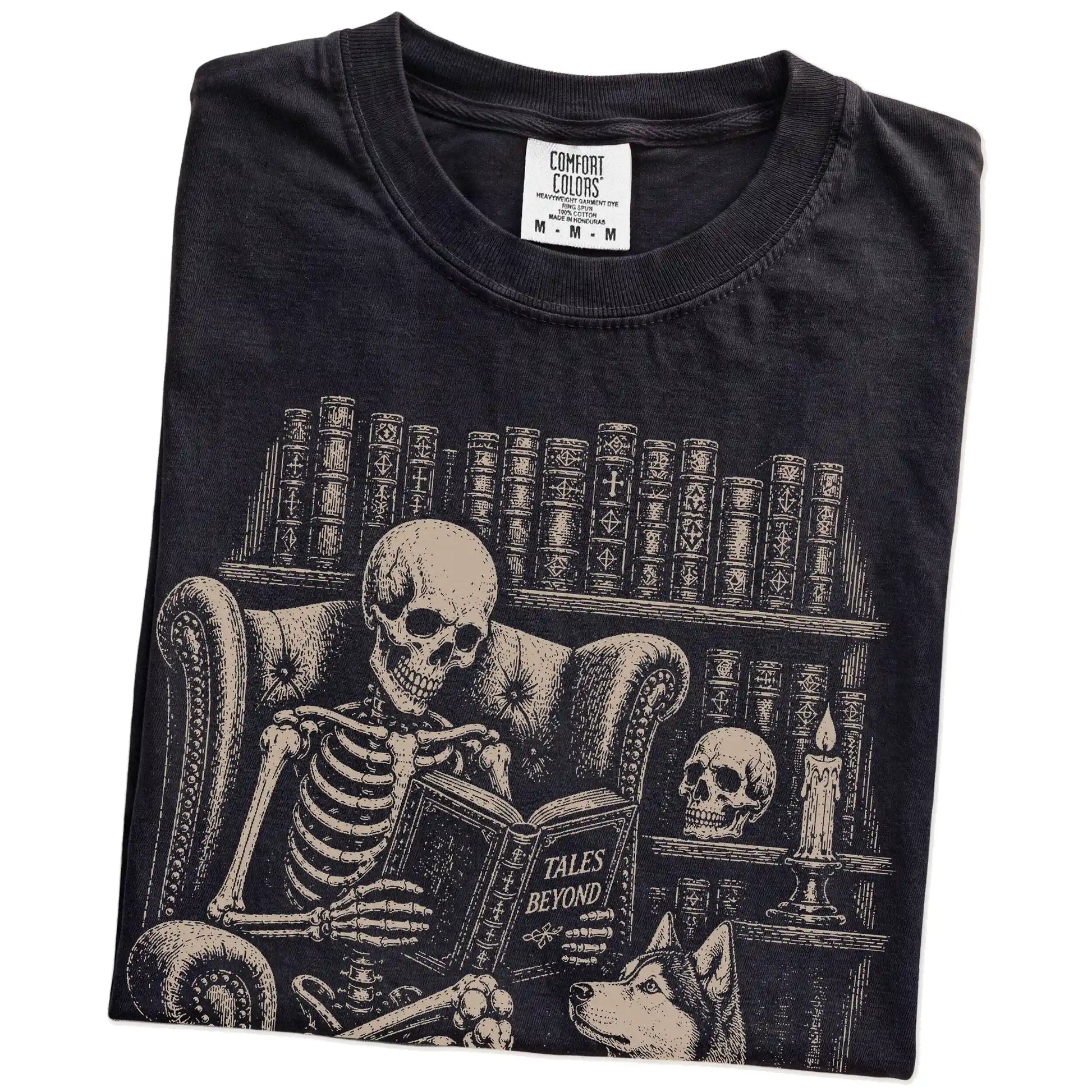Folded Black Comfort Colors® T-shirt showing skeleton reading in a library beside a Husky