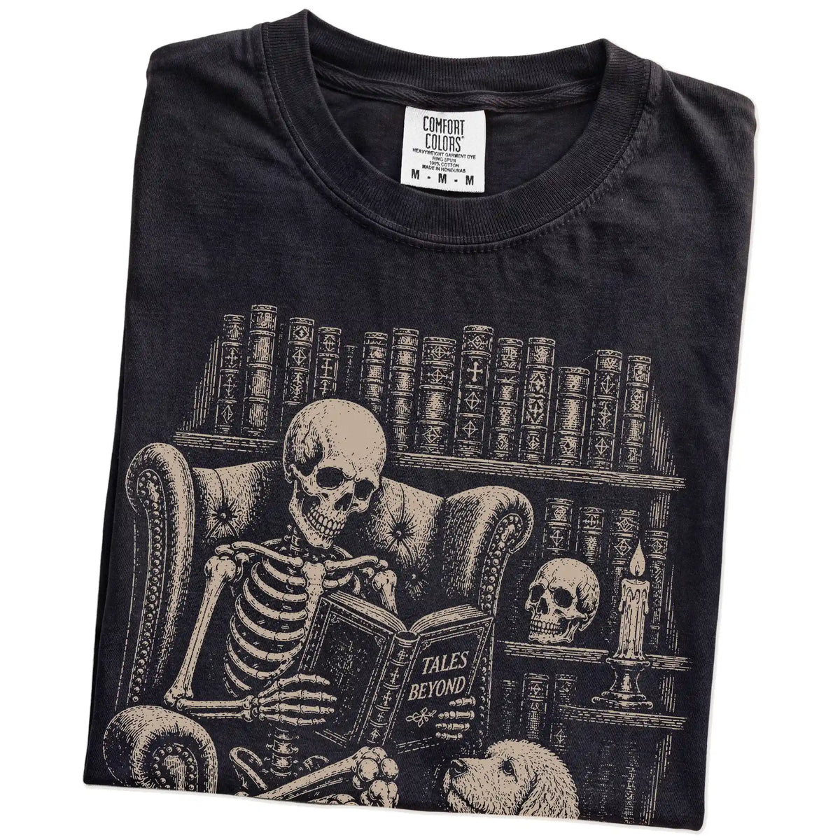 Folded Black Comfort Colors® T-shirt showing skeleton reading in a library beside a Labradoodle