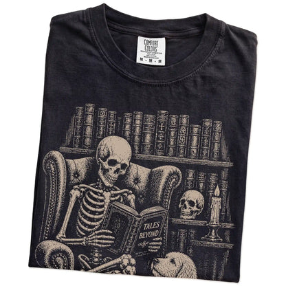 Folded Black Comfort Colors® T-shirt showing skeleton reading in a library beside a Labradoodle