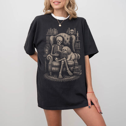 Model wearing a Black Comfort Colors® T-shirt showing skeleton reading in a library beside a Shih Tzu
