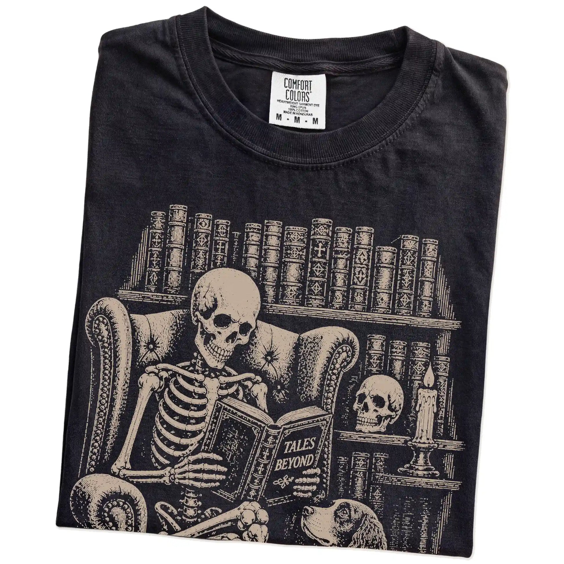 Folded Black Comfort Colors® T-shirt showing skeleton reading in a library beside a Springer Spaniel