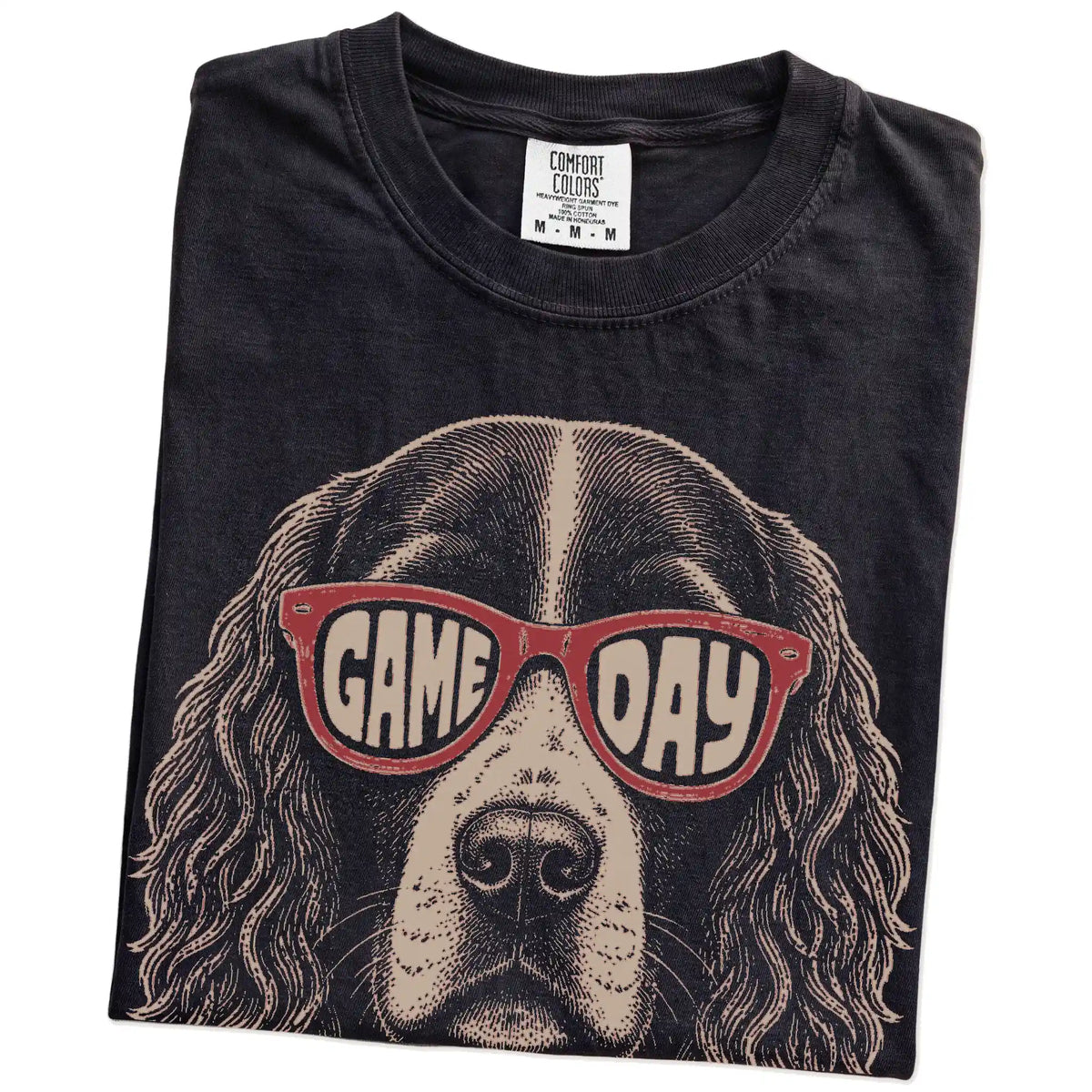 Folded Black Comfort Colors® T-shirt showing springer spaniel wearing red game day sunglasses