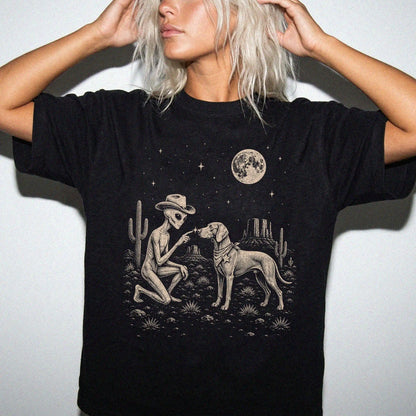 Model wearing a Black Comfort Colors® T-shirt with cowboy alien fist-bumping a weimaraner beneath the moon