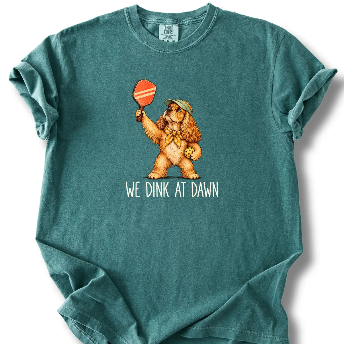 Cocker Spaniel with a pickleball paddle and ball on a Blue Spruce Comfort Colors® T-shirt with We Dink at Dawn text