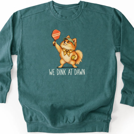 Pomeranian with a pickleball paddle and ball on a Blue Spruce Comfort Colors® sweatshirt with We Dink at Dawn text