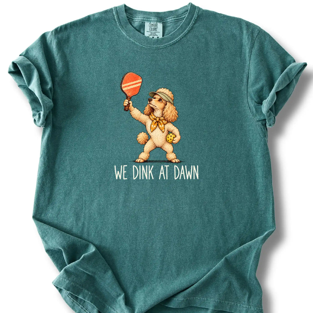 Poodle with a pickleball paddle and ball on a Blue Spruce Comfort Colors® T-shirt with We Dink at Dawn text