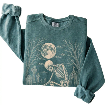 Folded Blue Spruce sweatshirt with a skeleton petting a Bichon Frise in a graveyard