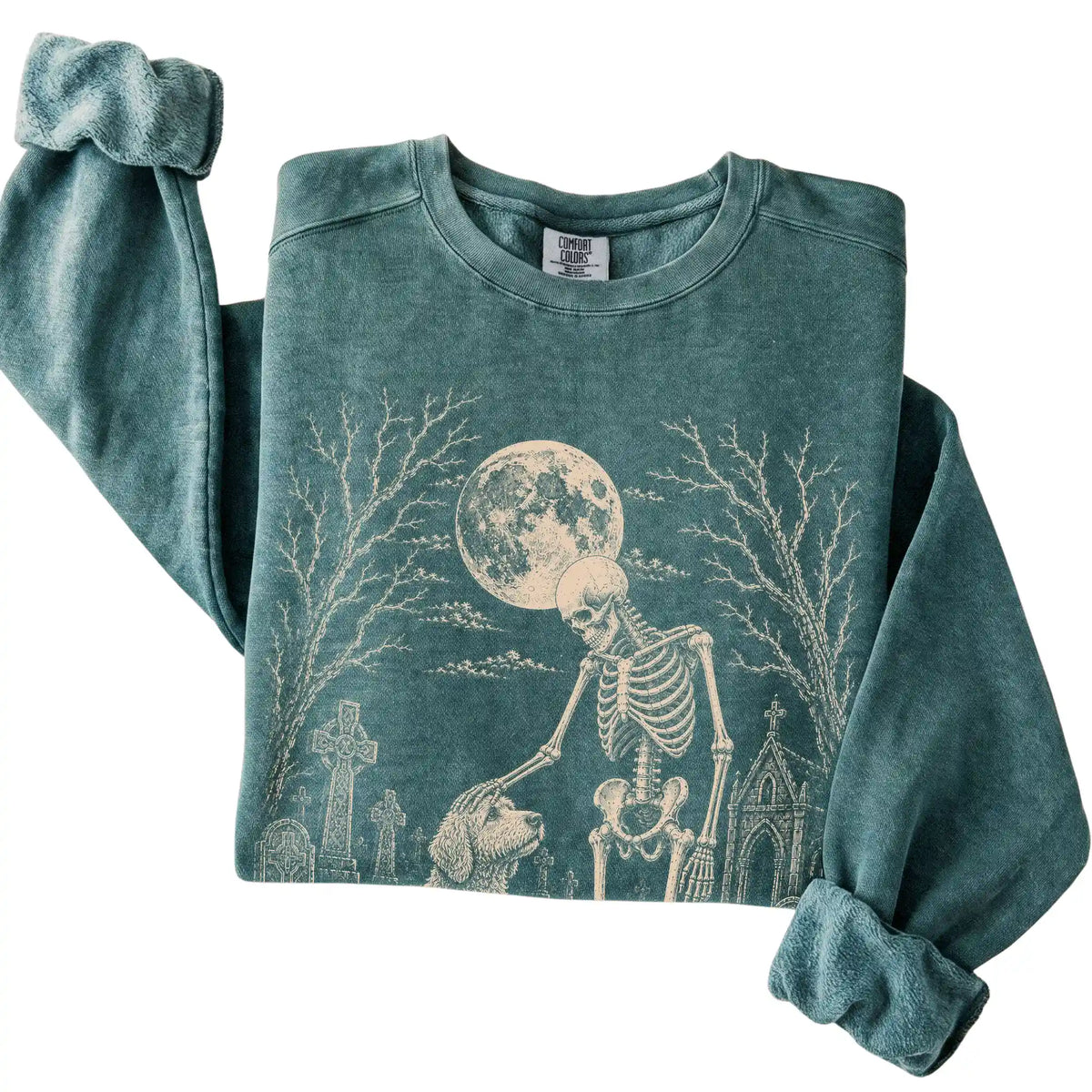Folded Blue Spruce sweatshirt with a skeleton petting a Goldendoodle in a graveyard