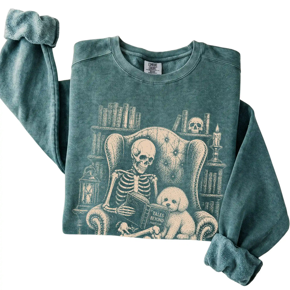 Folded Blue Spruce sweatshirt with a skeleton reading Tales Beyond to a Bichon Frise