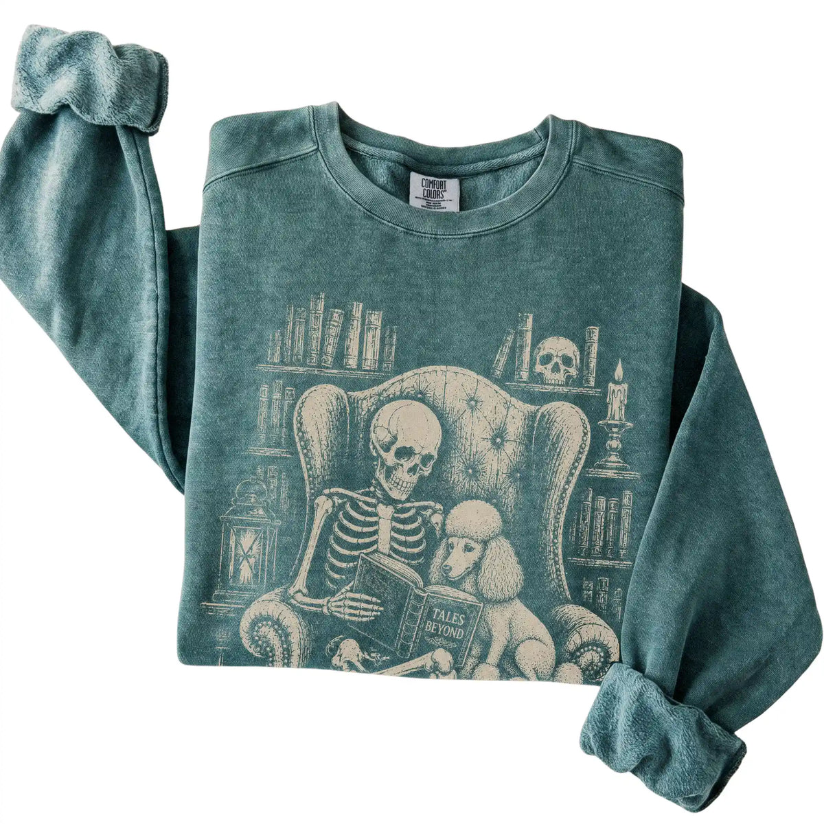 Folded Blue Spruce sweatshirt with a skeleton reading Tales Beyond to a Poodle