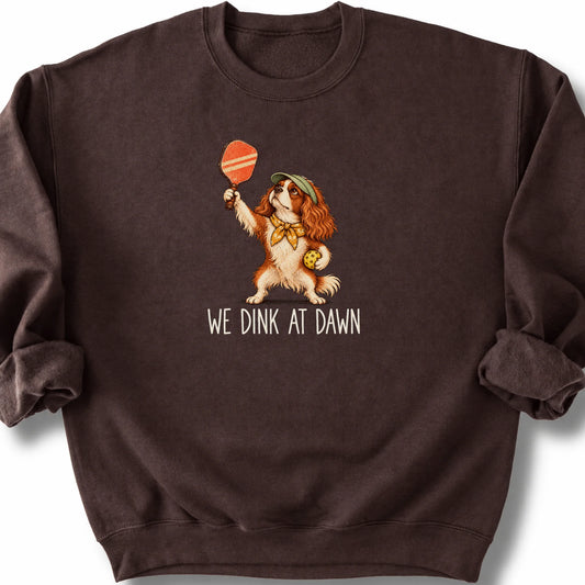 Cavalier with a pickleball paddle and ball on a Dark Chocolate Gildan® sweatshirt with We Dink at Dawn text
