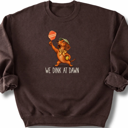 Dachshund with a pickleball paddle and ball on a Dark Chocolate Gildan® sweatshirt with We Dink at Dawn text