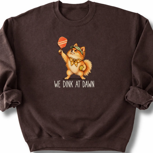 Pomeranian with a pickleball paddle and ball on a Dark Chocolate Gildan® sweatshirt with We Dink at Dawn text