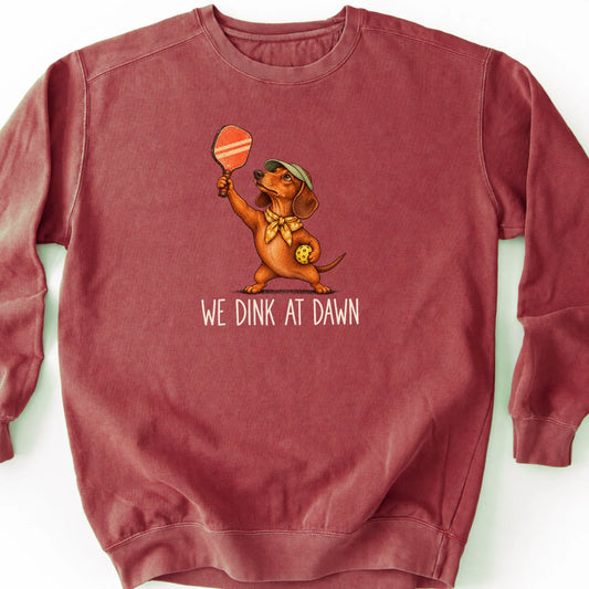 Dachshund with a pickleball paddle and ball on a Crimson Comfort Colors® sweatshirt with We Dink at Dawn text
