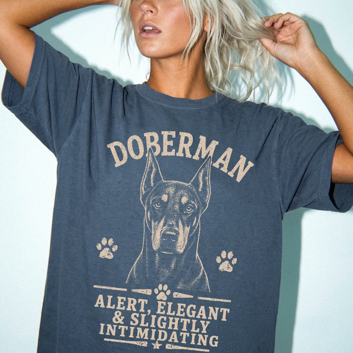 Model wearing a Denim Comfort Colors® T-shirt featuring Doberman design with “Alert, Elegant & Slightly Intimidating” letteri