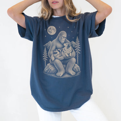 Person wearing a Denim T-shirt with Bigfoot holding an Australian Shepherd