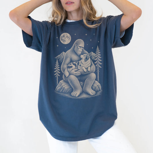 Person wearing a Denim T-shirt with Bigfoot holding an Australian Shepherd