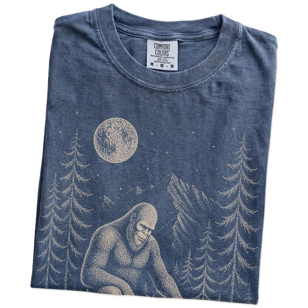 Folded Denim Comfort Colors® T-shirt showing bigfoot petting a basset hound beneath the moon in a pine forest